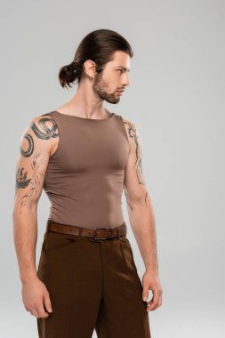 Side view of tattooed and long haired model looking away isolated on grey 