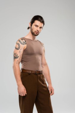 Bearded and tattooed man in sleeveless short looking at camera isolated on grey  clipart