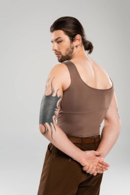 Long haired and tattooed man in tank top standing isolated on grey  clipart