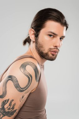 Portrait of long haired tattooed model looking at camera isolated on grey  clipart