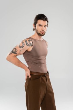 Stylish tattooed man in pants and tank top posing isolated on grey 