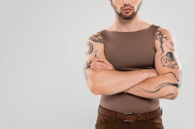 Cropped view of bearded tattooed man crossing arms isolated on grey  clipart