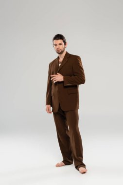 Full length of trendy man in brown suit standing on grey background