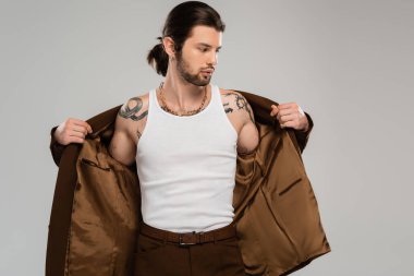 Long haired tattooed man wearing jacket isolated on grey  clipart