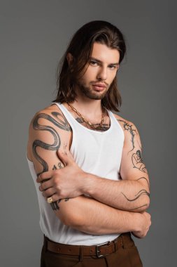 Fashionable and tattooed man in tank top posing isolated on grey  clipart