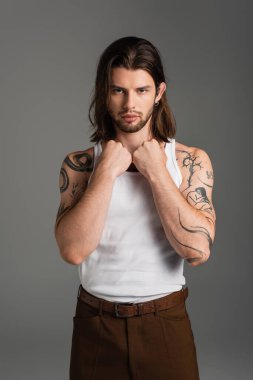 Stylish long haired model with tattoo on body looking at camera isolated on grey 