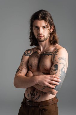 Muscular tattooed model posing while standing isolated on grey 