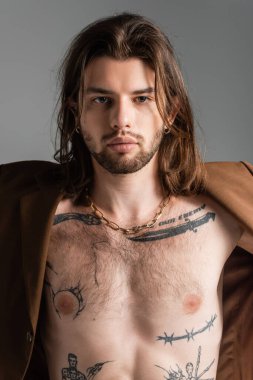 Tattooed and long haired man in jacket standing isolated on grey 