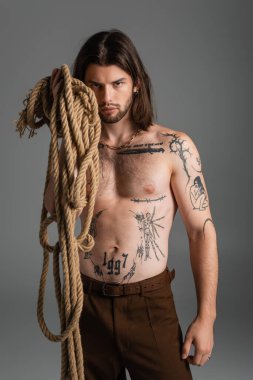 Shirtless tattooed man holding rope isolated on grey 