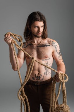 Sexy tattooed man holding rope isolated on grey 
