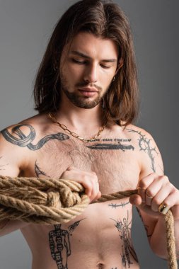 Sexy and tattooed man holding rope isolated on grey 