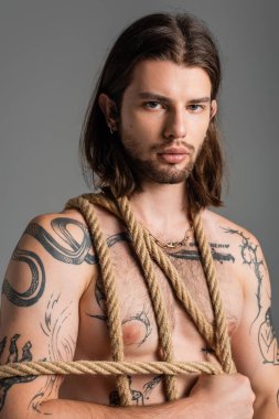 Portrait of sexy tattooed man holding rope isolated on grey 