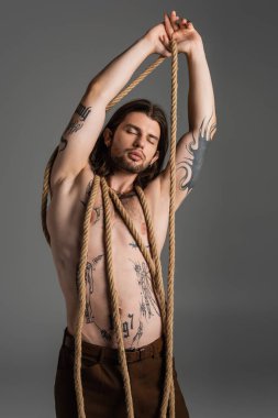 Muscular tattooed model posing with rope isolated on grey 