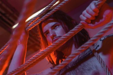 Low angle view of tattooed man holding ropes with lighting 