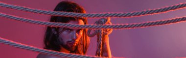 Long haired man holding rope on purple background with light, banner 