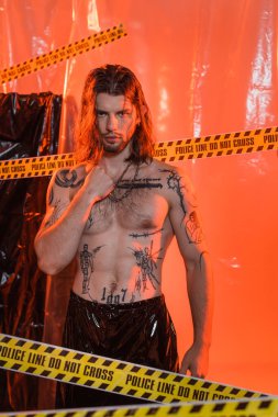 Muscular tattooed man looking at camera near police line and cellophane 