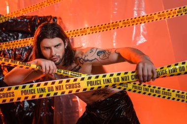 Shirtless tattooed man touching police line near cellophane at background 