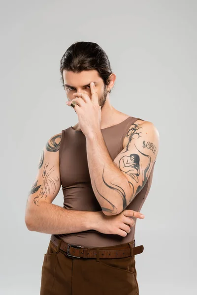 Brunette tattooed man touching eyebrow isolated on grey