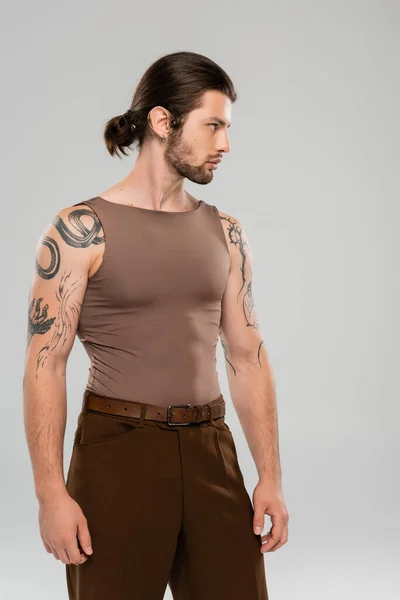 Side view of tattooed and long haired model looking away isolated on grey