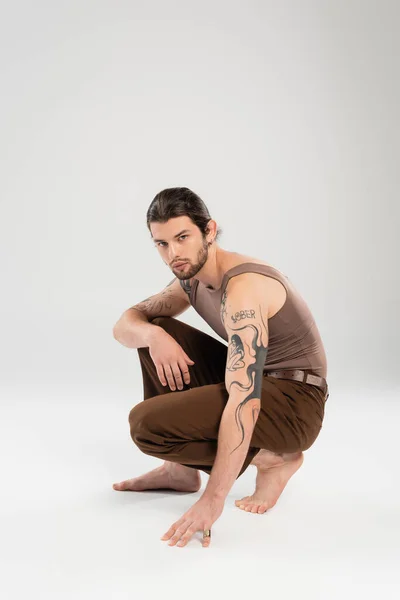 Full length of tattooed and barefoot man posing on grey background