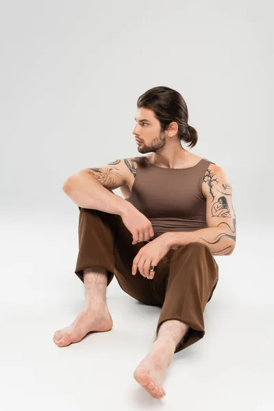 Side view of tattooed and long haired man sitting on grey background