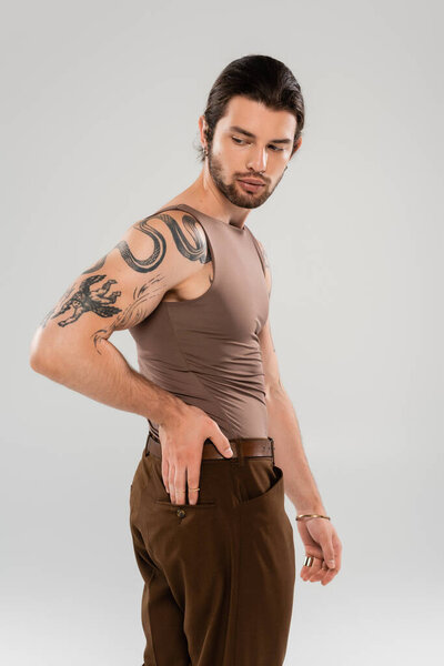 Brunette bearded man with tattoo posing isolated on grey 
