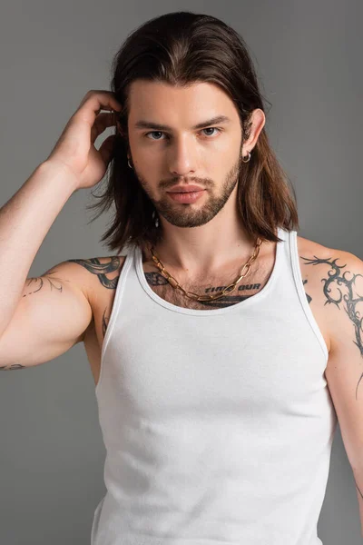 Portrait of young man with tattoo touching hair isolated on grey