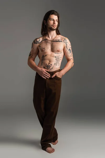 Full length of tattooed and shirtless man with tattoo on body on grey background