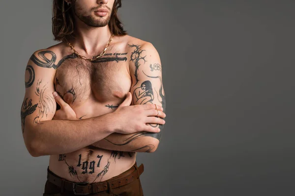 Cropped view of long haired and tattooed man crossing arms isolated on grey