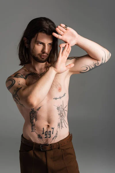 Bearded long haired model with tattoo on torso posing isolated on grey