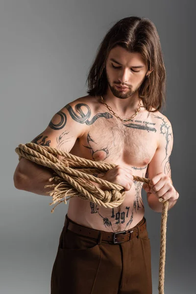 Shirtless and tattooed model holding rope isolated on grey