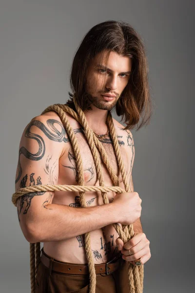Long haired and tattooed model holding rope isolated on grey