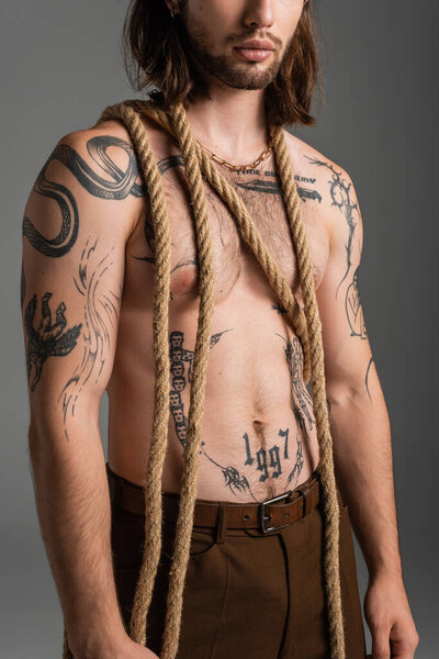 Cropped view of bearded and tattooed man with rope isolated on grey 