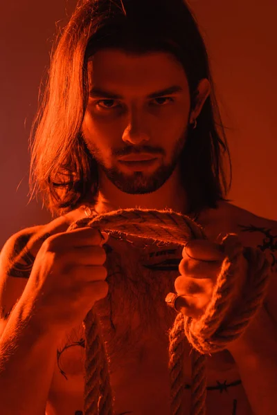 Portrait of tattooed man holding rope isolated on red 