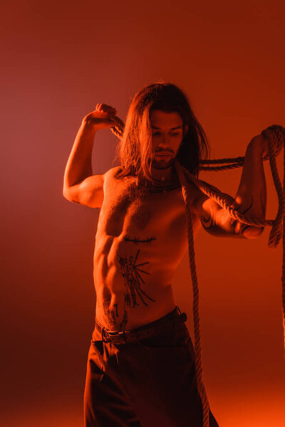 Sexy tattooed model holding rope isolated on red with light 