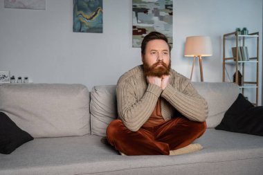 Oturma odasındaki kanepede oturan hırkalı adam. 