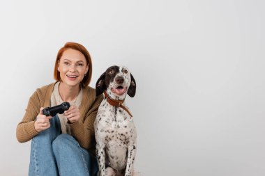 KYIV, UKRAINE - 16 Aralık 2022: Dalmaçyalı köpeğin yanında video oyunu oynayan gülümseyen kızıl saçlı kadın 