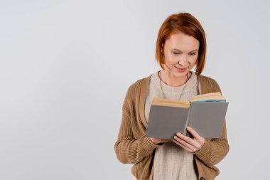 Gülümseyen kızıl saçlı kadın kitap okuyor. 