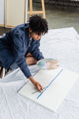 Genç Afro-Amerikan ressamın atölyedeki tuvale çizdiği yüksek açılı manzara 