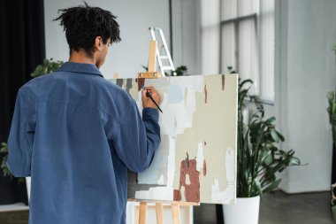 Back view of african american man painting on canvas in studio  clipart