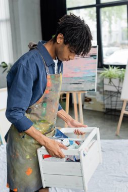 Afrikalı Amerikalı ressam, stüdyo boyalarıyla dolu bir kutu tutuyor. 