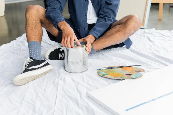 Stock image Cropped view of african american artist opening jar with paint near canvas and palette in workshop 