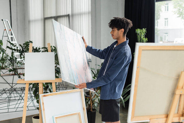 Side view of african american artist looking at painting in workshop