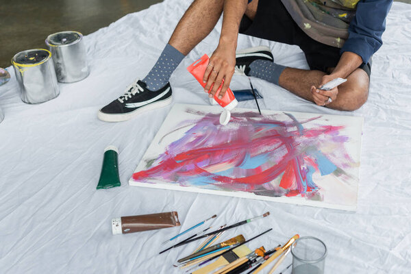 Cropped view of african american artist pouring paint on canvas on cloth in studio 