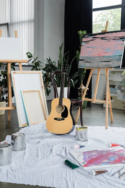 Acoustic guitar near paintings and paints in studio
