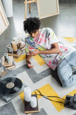 Stüdyoda müzik çaları ve kitapların yanında akıllı telefon kullanan Afrikalı Amerikalı bir sanatçının yüksek açılı görüntüsü 