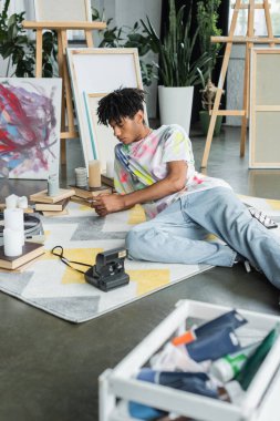Afrikalı Amerikalı ressam cep telefonunu klasik kamera ve kitapların yanında kullanıyor. 