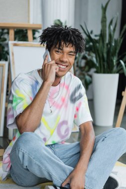 Gülümseyen Afrikalı Amerikalı sanatçı atölyede akıllı telefondan konuşuyor. 