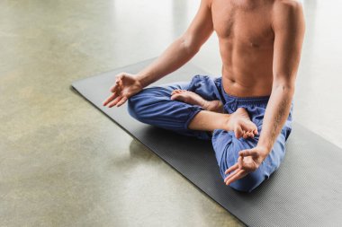 cropped view of man in blue pants sitting in lotus pose and doing gyan mudra  clipart