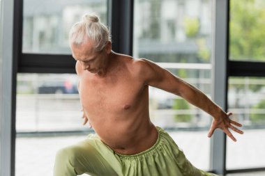 Yeşil pantolonlu üstsüz adam yoga stüdyosunda hilal hamlesi yapıyor. 